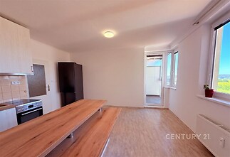 Moderní kuchyň s dřevěnými pracovními deskami, světlá parketová podlaha, velká okna poskytující dostatek světla.
