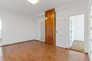 Prázdný obývací pokoj s dlažbou a dřevěným obkladem, vedoucí do moderního interiéru, světlý prostor s bílými dveřmi, připraven k transformaci