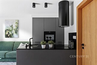 Moderní kuchyň s černým vybavením, minimalistickými skříňkami a vestavěnou troubou, parketová podlaha a světlé stěny.