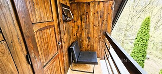 Balkon s dřevěným obložením, parketovou podlahou a výhledem na zahradu, nabízí útulný venkovský styl a soukromí pro relaxaci.