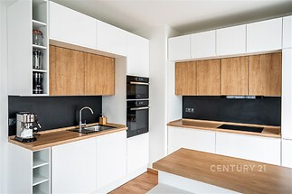 Moderní kuchyň s dřevěnými prvky, vestavěnými spotřebiči a čistým bílým designem, parketová podlaha zvýrazňuje elegantní styl.