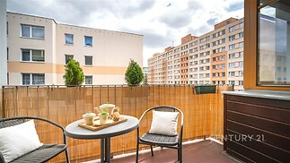Balkon s dlažbou, vybavený venkovním posezením a výhledem na okolní bytové domy, nabízí příjemný prostor k relaxaci.