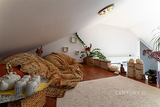 Podkrovní pokoj s dřevěnou podlahou, útulným designem a dekorativními prvky. Světlé stěny a střešní okno poskytují dostatek přirozeného světla.