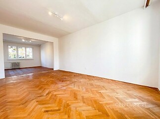 Světlý obývací pokoj s parketovou podlahou, velkými okny a bílými stěnami, moderní a prostorný, ideální pro rodinné bydlení