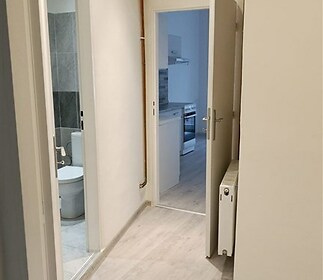 Chodba s moderními parketovými podlahami, vede do koupelny s dlažbou a světlé kuchyně.