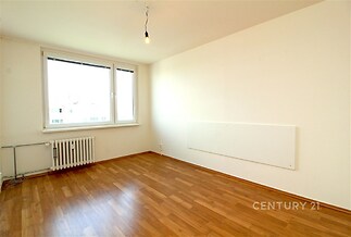 Světlý obývací pokoj s parketovou podlahou, velká okna poskytující dostatek přirozeného světla, moderní minimalistický styl.