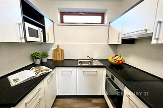 Moderní kuchyň s bílými skříňkami, černou pracovní deskou a vestavěnými spotřebiči, světlý prostor s parketovou podlahou