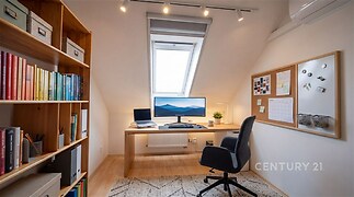 Podkrovní pracovna s parketovou podlahou, vestavěnými skříněmi, moderní osvětlení a velké střešní okno zajišťující světlý interiér.