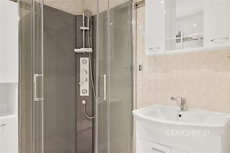 Moderní koupelna s proskleným sprchovým koutem, světlá dlažba a bílá umyvadlová skříňka, elegantní a čistý design.