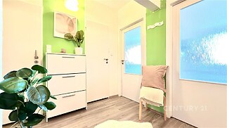 Světlá předsíň s laminátovou podlahou, moderním nábytkem a dekorativními prvky, jako jsou velká zrcadla a živé rostliny.