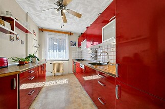 Moderní kuchyň s červenými skříněmi, dřevěnými pracovními deskami a velkým oknem, dlažba na podlaze, světlý prostor, retro styl.