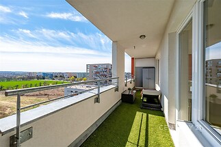Prostorný balkon s umělým trávníkem, moderním zábradlím a panoramatickým výhledem na město, ideální pro relaxaci v příjemném prostředí.