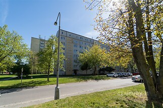Panelový bytový dům obklopený zelení, s parkovacími místy u přední části budovy, v klidné a dobře dostupné lokalitě.