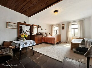 Prostorná ložnice s dřevěným stropem a parketovou podlahou, velká okna poskytují světlé prostředí, historický nábytek dodává rustikální atmosféru.