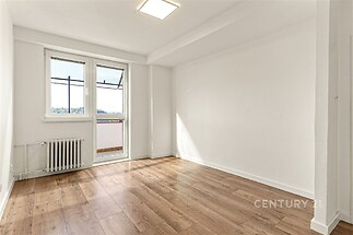 Světlý obývací pokoj s parketovou podlahou, velká okna zajišťují dostatek přirozeného světla, moderní čistý design