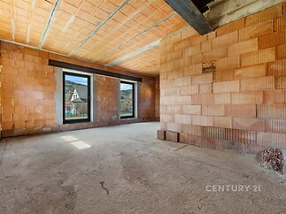 Nedokončený obývací pokoj s betónovou podlahou, velká okna poskytují přirozené světlo, prostor pro moderní design interiéru