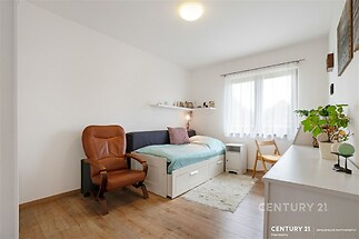 Světlá ložnice s parketovou podlahou, velkým oknem a moderním nábytkem nabízí komfortní prostor pro odpočinek.