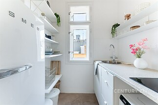 Úzká moderní kuchyň s bílou linkou, vestavěným dřezem a velkými okny, vybavená parketovou podlahou a stylovou dekorací.