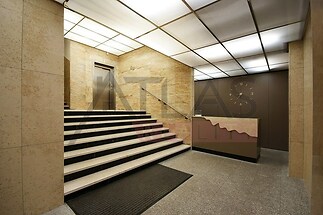 Elegantní vstupní hala s mramorovými obklady, moderními svítidly a kovovými prvky. Luxusní dojem podtrhuje světlá dlažba a stylové schodiště.