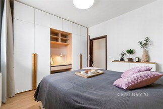 Moderní ložnice s parketovou podlahou, vestavěnými skříněmi a světlým nábytkem, ideální pro pohodlné bydlení.