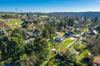 Pohled na malebnou vesnici obklopenou přírodou s rodinnými domy a zahradami, moderní i tradiční architektura, klidné prostředí.