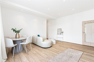 Světlý obývací pokoj s parketovou podlahou, moderní nábytek a minimalistický styl, nabízí prostor pro setkání a relaxaci.