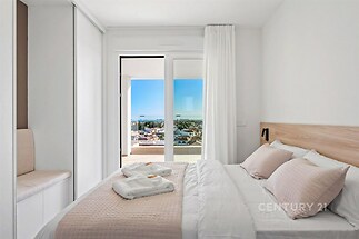 Světlá ložnice s velkými okny, nabízející úchvatný výhled. Moderní vestavěné skříně a dřevěné prvky dodávají prostoru elegantní styl.