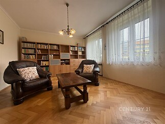 Světlý obývací pokoj s parketovou podlahou, velká okna, dřevěný nábytek, moderní styl, prostorné policové jednotky, pohodlná křesla.