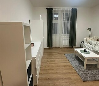 Světlý obývací pokoj s parketovou podlahou, moderním osvětlením a velkými okny, jednoduchý a útulný styl interiéru.