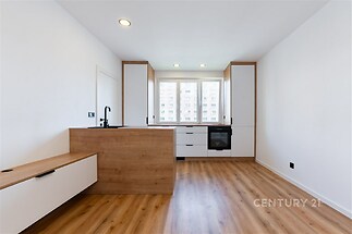 Kuchyň s dřevěnou podlahou, moderním designem a vestavěnými spotřebiči, světlý interiér s velkými okny zajišťujícími dostatek denního světla.