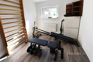 Domácí posilovna s moderním vybavením, dřevěnou parketovou podlahou a velkým oknem zajišťujícím dostatek přirozeného světla.