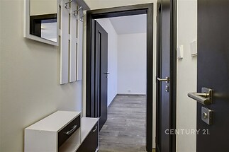 Vstupní chodba s moderními dveřmi, šatní skříní a světlou dlažbou, vedoucí do místnosti s dřevěnou podlahou.