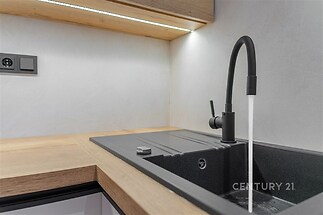 Moderní kuchyň s černým dřezem, matná baterie, dřevěná pracovní deska, úsporné LED osvětlení, stylový a elegantní design.