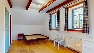 Prostorná ložnice s dřevěnou podlahou, velkými okny a dřevěnými trámy na stropě nabízí světlý interiér a útulnou atmosféru.