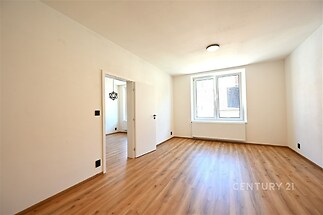 Světlý pokoj s parketovou podlahou, moderními dveřmi a velkými okny, které poskytují dostatek přirozeného světla.