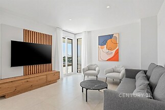 Světlý obývací pokoj s moderní dlažbou, velkými okny a elegantním nábytkem nabízí výhled a stylový umělecký prvek na stěně.