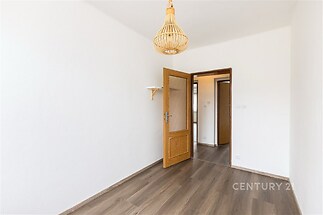 Prázdný pokoj s dřevěnou podlahou, dekorativním osvětlením a bílými stěnami, připravený k zařizování, moderní interiér a dveře s prosklením.