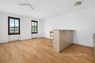 Světlý obývací pokoj s parketovou podlahou, velkými okny a moderním barem, ideální pro rekonstruovaný byt v městském stylu.