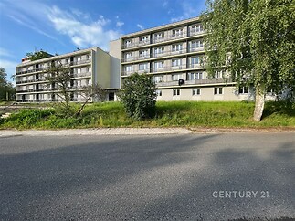 Vícepatrový bytový dům s balkony, obklopen zelení. Budova ve světlých barvách v klidné lokalitě, situována u asfaltové komunikace.