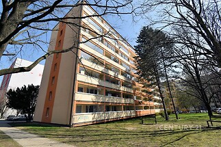 Panelový bytový dům se zateplenou fasádou a balkony, nacházející se v klidné části města, obklopený zelení a s parkovacími místy v okolí.