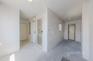 Světlá chodba ve fázi rekonstrukce s betonovou podlahou, velkými okny a moderním uspořádáním nabízí potenciál pro vestavěné skříně.