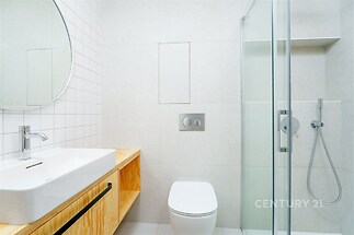 Moderní koupelna s dřevěným umyvadlovým pultem, skleněným sprchovým koutem a světlými dlaždicemi vytváří elegantní a čistý vzhled.