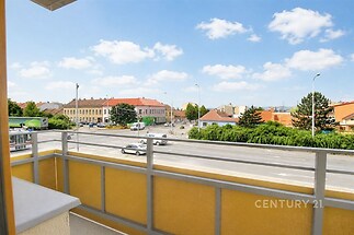 Prostorný balkon s výhledem na město, moderní zábradlí, slunečné počasí, klidná lokalita, ideální pro relaxaci venku.