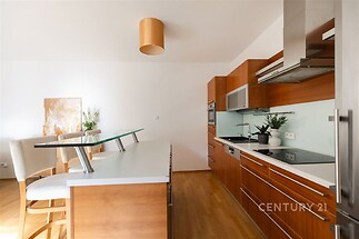 Moderní kuchyň s parketovou podlahou, vestavěné spotřebiče a ostrůvkem, světlý interiér s dřevěnými detaily.