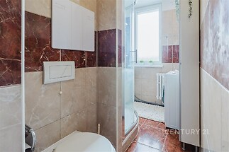 Kompaktní koupelna, dlažba s mramorovým vzorem, sprchový kout, světlé stěny, moderní vybavení, velké okno pro přirozené osvětlení.