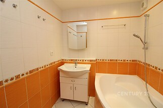 Koupelna s dlažbou, vanou a zrcadlem. Oranžové obklady dodávají moderní vzhled. Vhodná pro rodiny i jednotlivce.