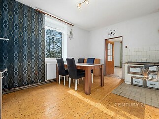 Světlá jídelna s korkovou podlahou, velká okna propouštějí přirozené světlo, vedle moderní kuchyně s původními kamny.