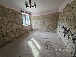Nedokončený pokoj s odkrytými kamennými zdmi, světlý díky velkému oknu, vhodný k rekonstrukci, potenciál pro moderní úpravy.