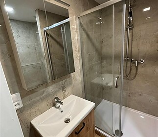 Koupelna s moderním sprchovým koutem, parketovou podlahou a světlými keramickými obklady, elegantní dřevěná skříňka pod umyvadlem