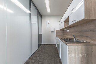 Moderní kuchyň s dřevěnou pracovní deskou, světlými skříňkami a vestavěnými spotřebiči. Skleněná příčka a koberec dodávají elegantní vzhled.